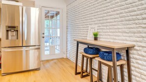 Una cucina con un frigorifero in acciaio inossidabile, un tavolo di legno con cuscini blu e una parete in mattoni bianchi.