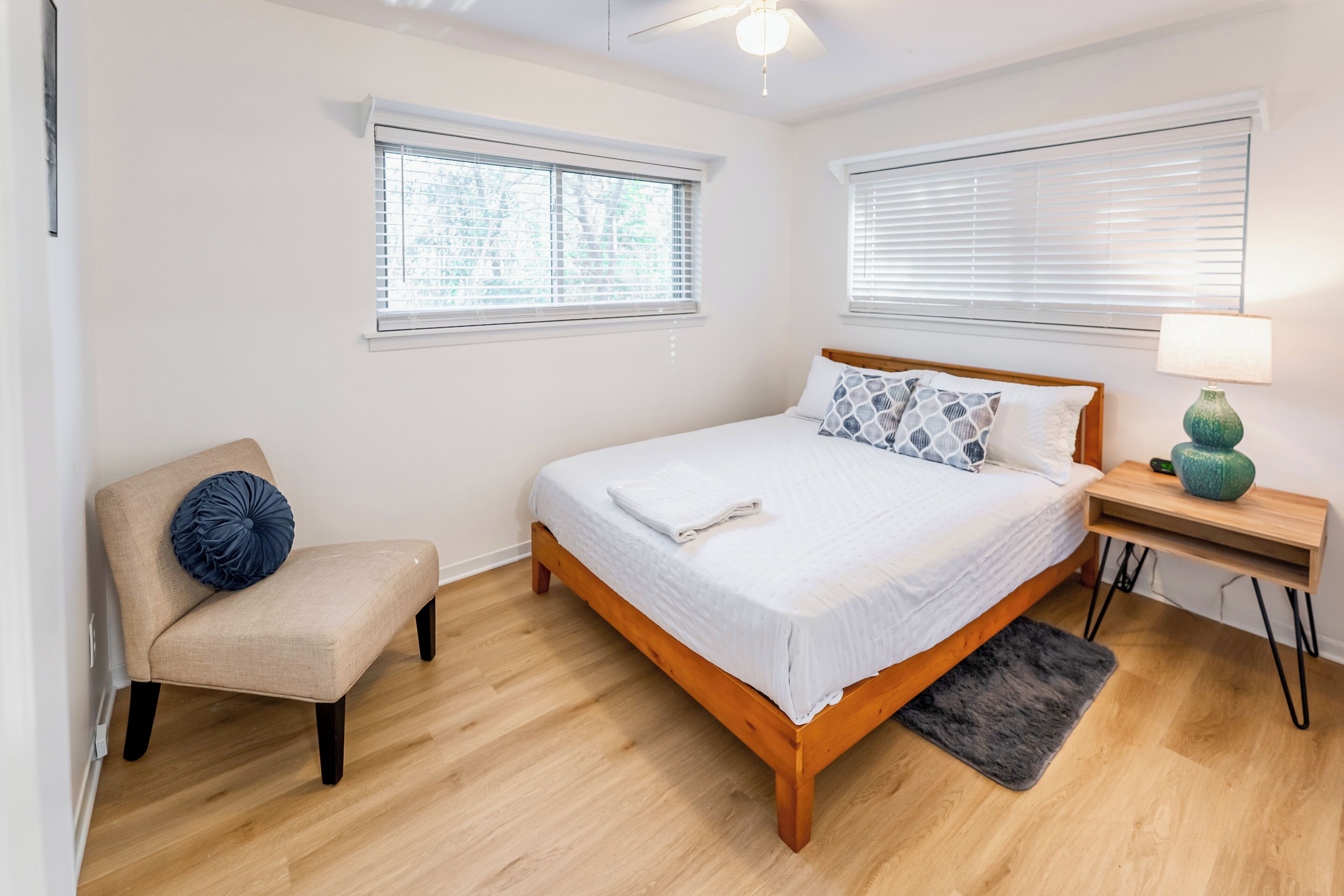 A bedroom with a bed, a chair, a nightstand, and two windows.