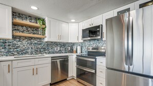 A modern kitchen with white cabinets, stainless steel appliances, and a tiled backsplash. - Steps to Sand! 8th-floor North Myrtle Beach Condo (North Myrtle Beach)