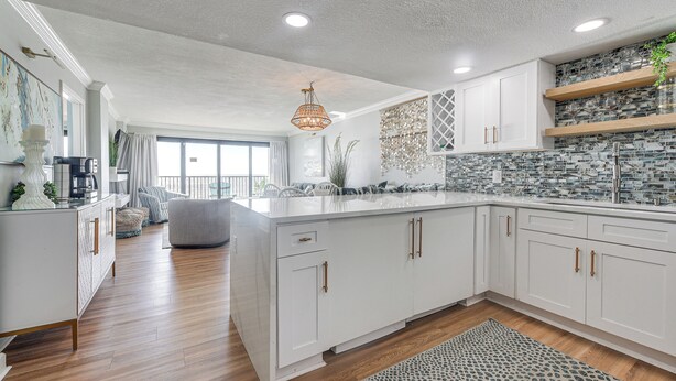 A modern kitchen with white cabinetry, a large island, and a patterned backsplash. - Steps to Sand! 8th-floor North Myrtle Beach Condo (North Myrtle Beach)