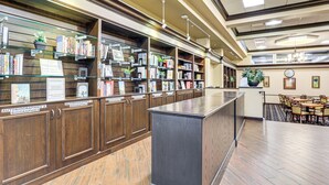 Une bibliothèque avec des étagères en bois, un bureau central et un espace repas avec des tables et des chaises.