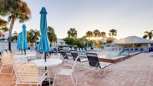 Un espace aménagé au bord de la piscine, avec des chaises longues et des parasols, une piscine et des palmiers.