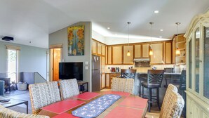 A spacious dining area with a long table and wicker chairs, a kitchen with wooden cabinets and modern appliances, and a large painting on the wall. - Walk to Main St Frisco: Mount Royal View (Frisco)