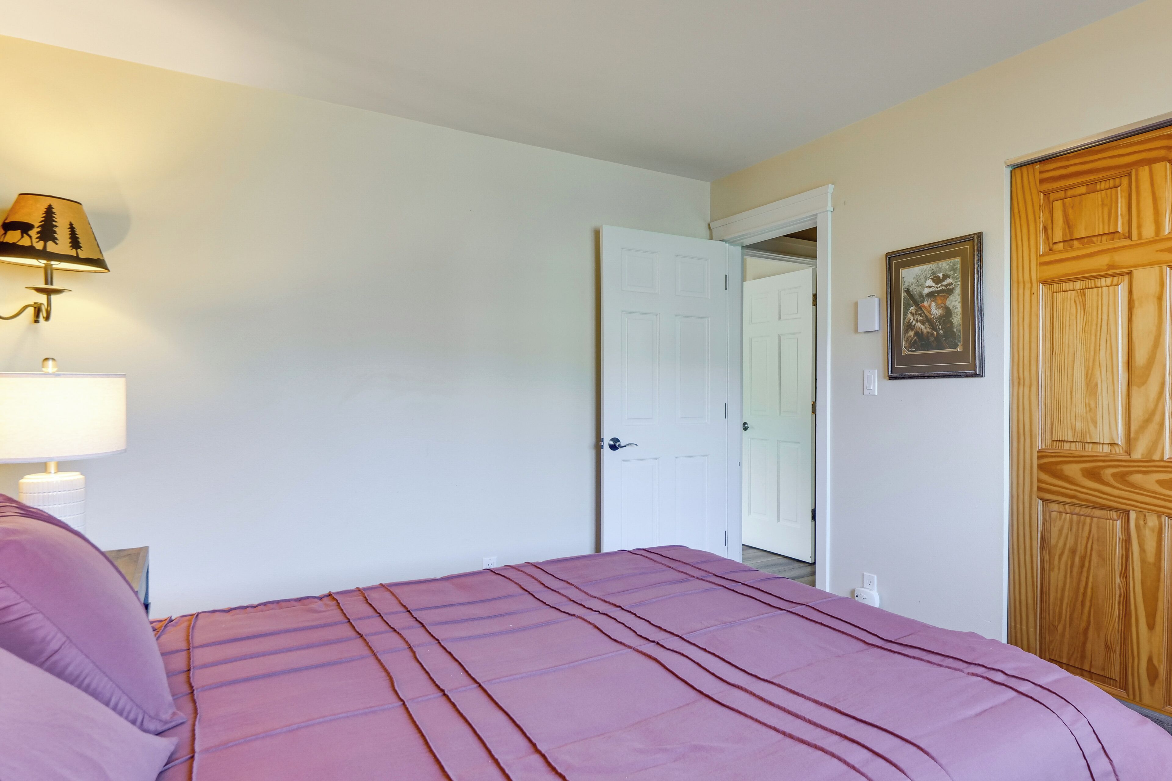 A bedroom with a bed, a nightstand, a lamp, a door, and a wooden wardrobe.