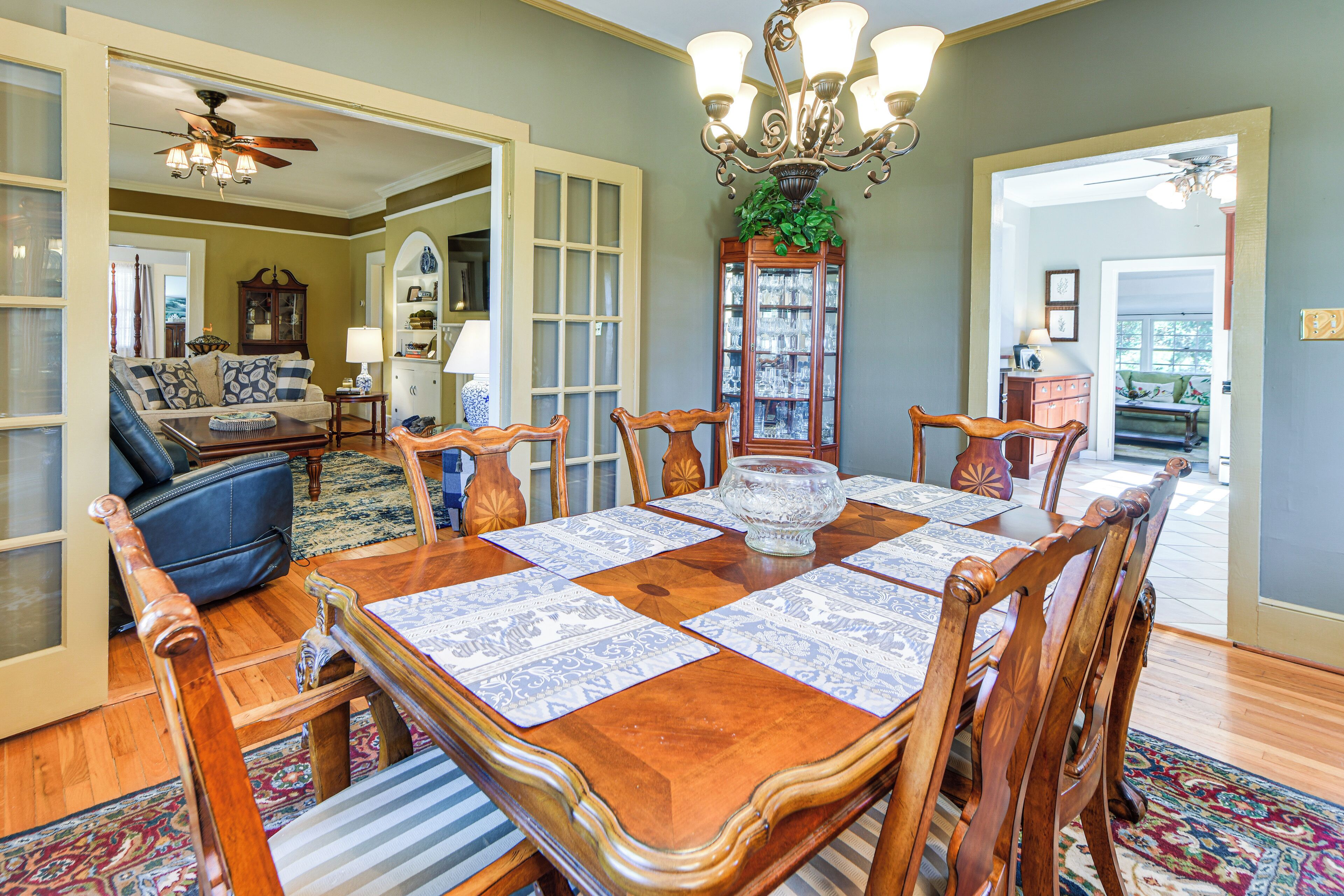 A dining room with a wooden table set for six, surrounded by chairs.