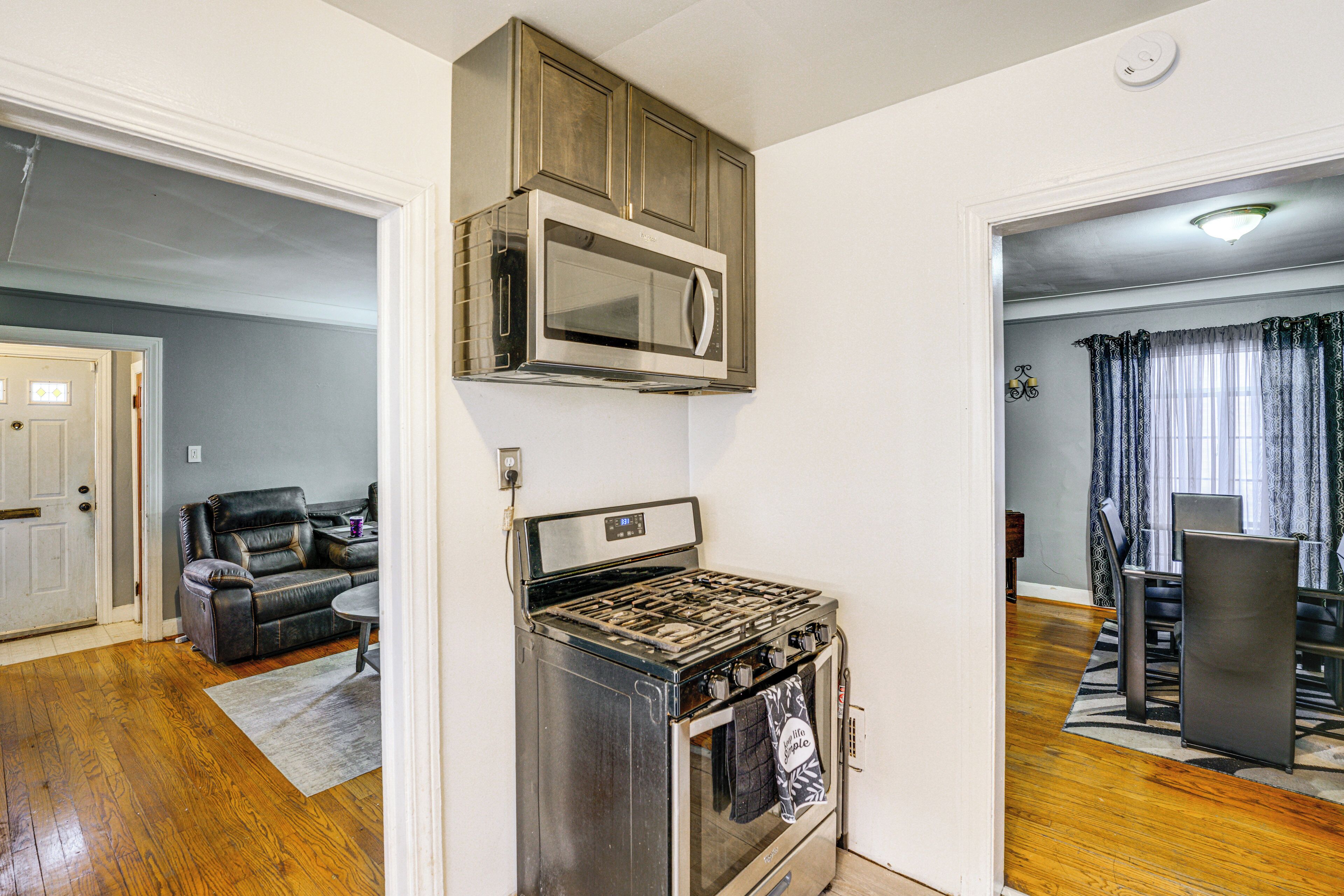 A kitchen with a stove, oven, and microwave. There is a dining table and chairs in the adjacent room.