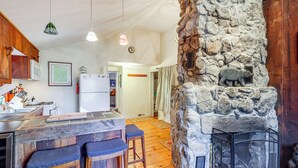 A kitchen with wooden cabinets, a refrigerator, and a stone wall with a bear sculpture. - 4 Mi to Stratton Mountain Resort! Cabin w/ Hot Tub (Jamaica)