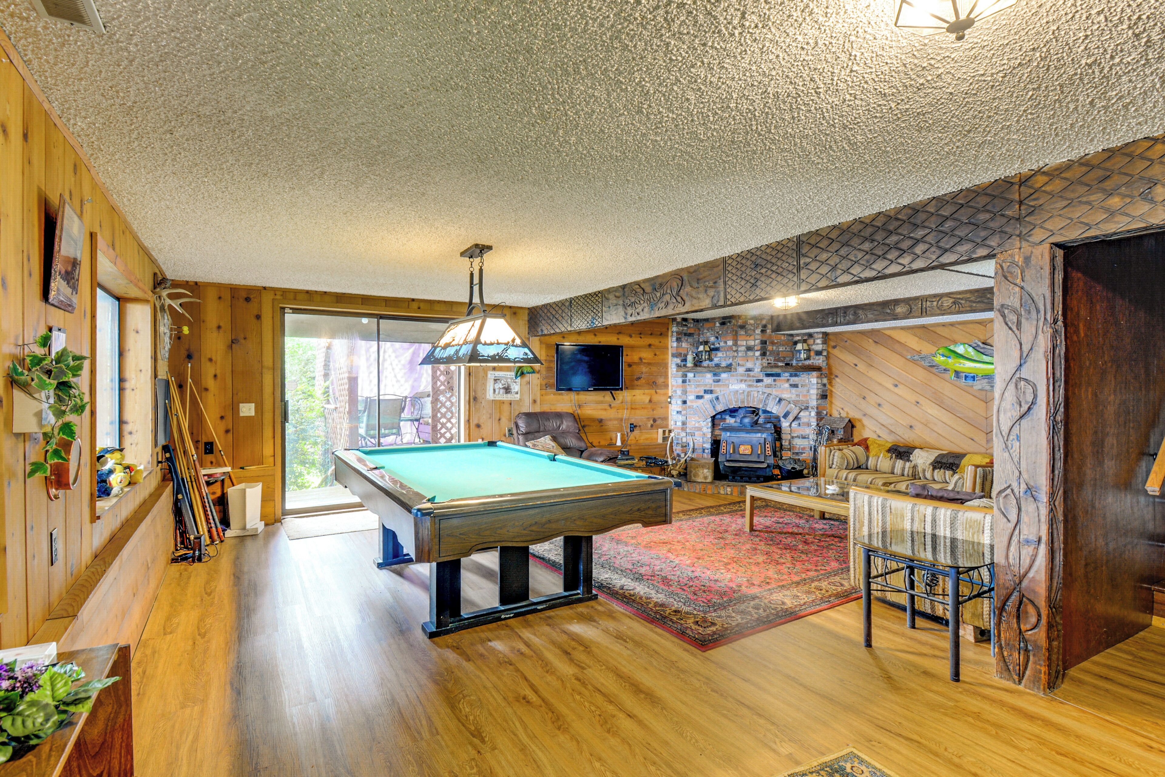 A wooden-floored room with a pool table, a fireplace, and a television.