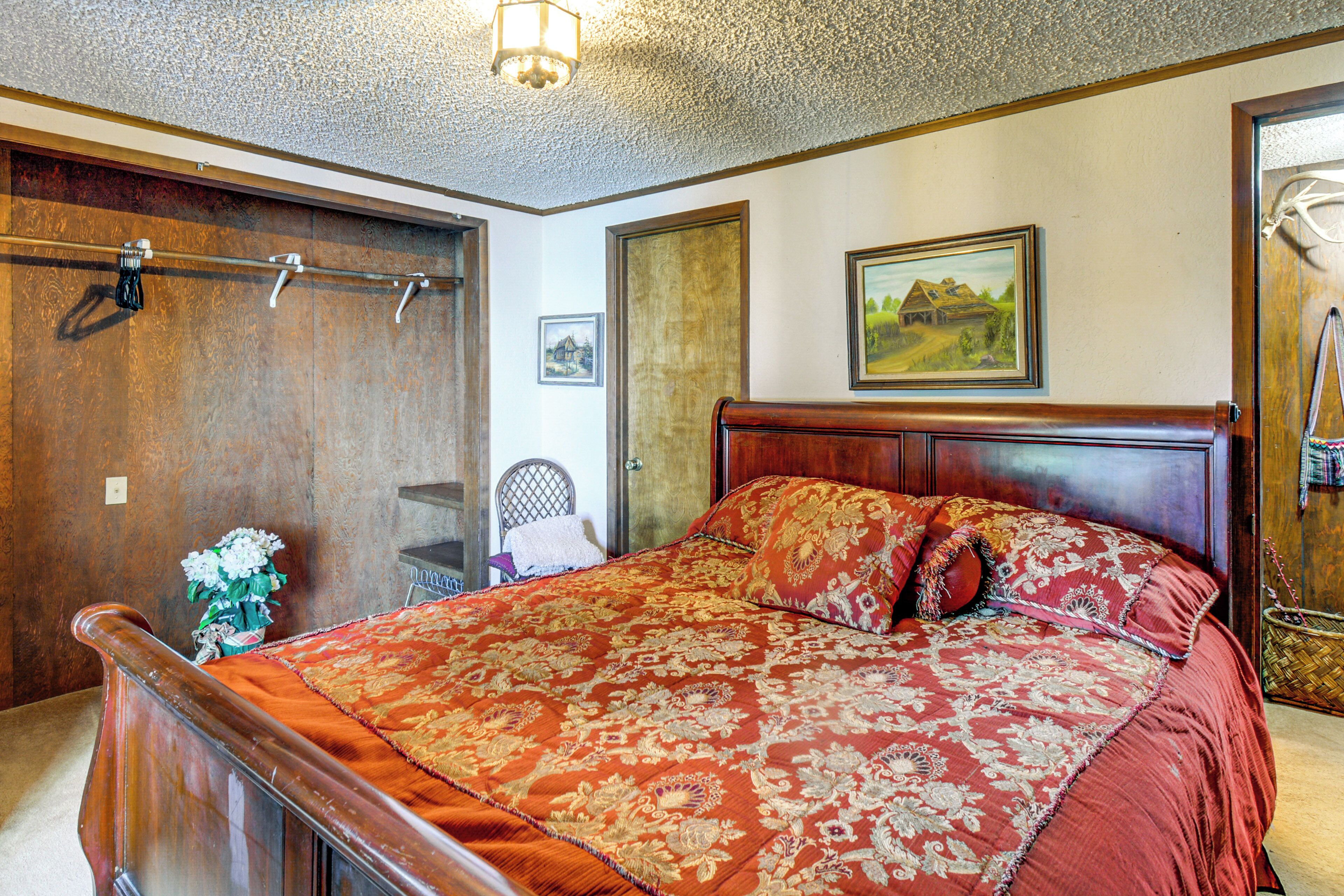 A bedroom with a wooden bed, a wooden headboard, a painting on the wall, and a door with a coat hanging on it.