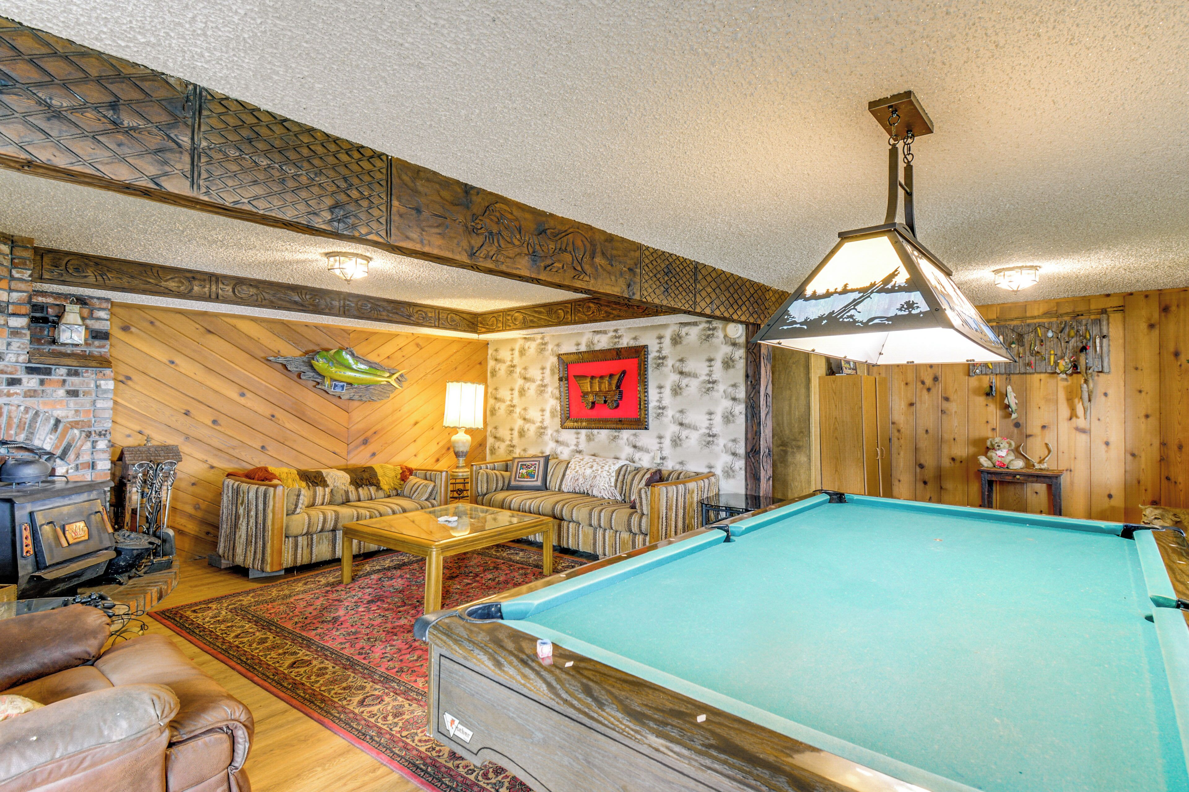 A cozy room with a pool table, a sofa, a fireplace, and a wooden ceiling.