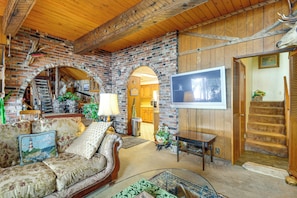 Ein gemütliches Wohnzimmer mit Kamin aus Ziegelsteinen, einer bequemen Couch, einem Fernseher und einer Treppe, die in eine weitere Ebene führt.