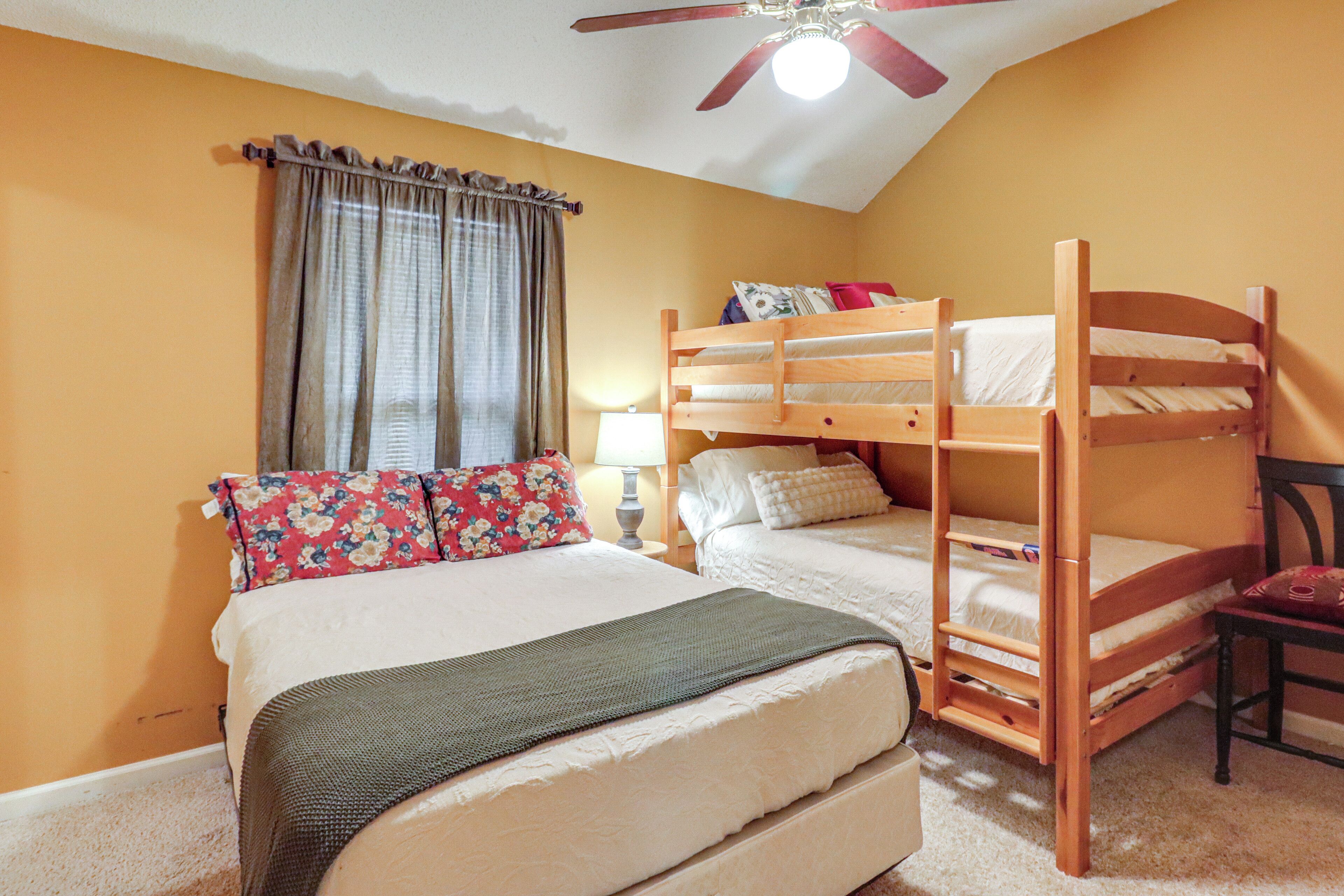 A room with a bunk bed, a single bed, a ceiling fan, a window with curtains, and a lamp.