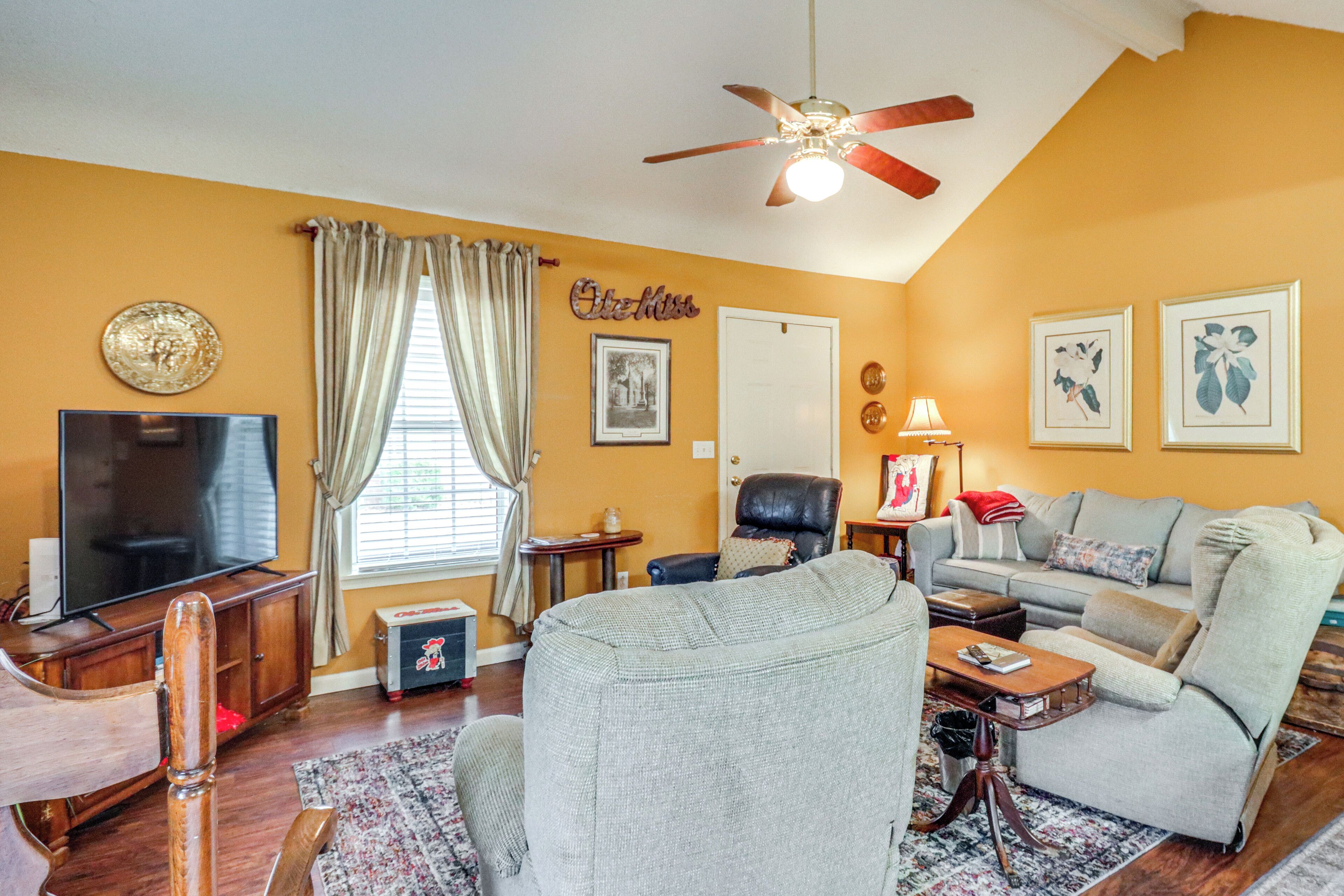 A living room with a television, a ceiling fan, a sofa, a chair, and a coffee table.