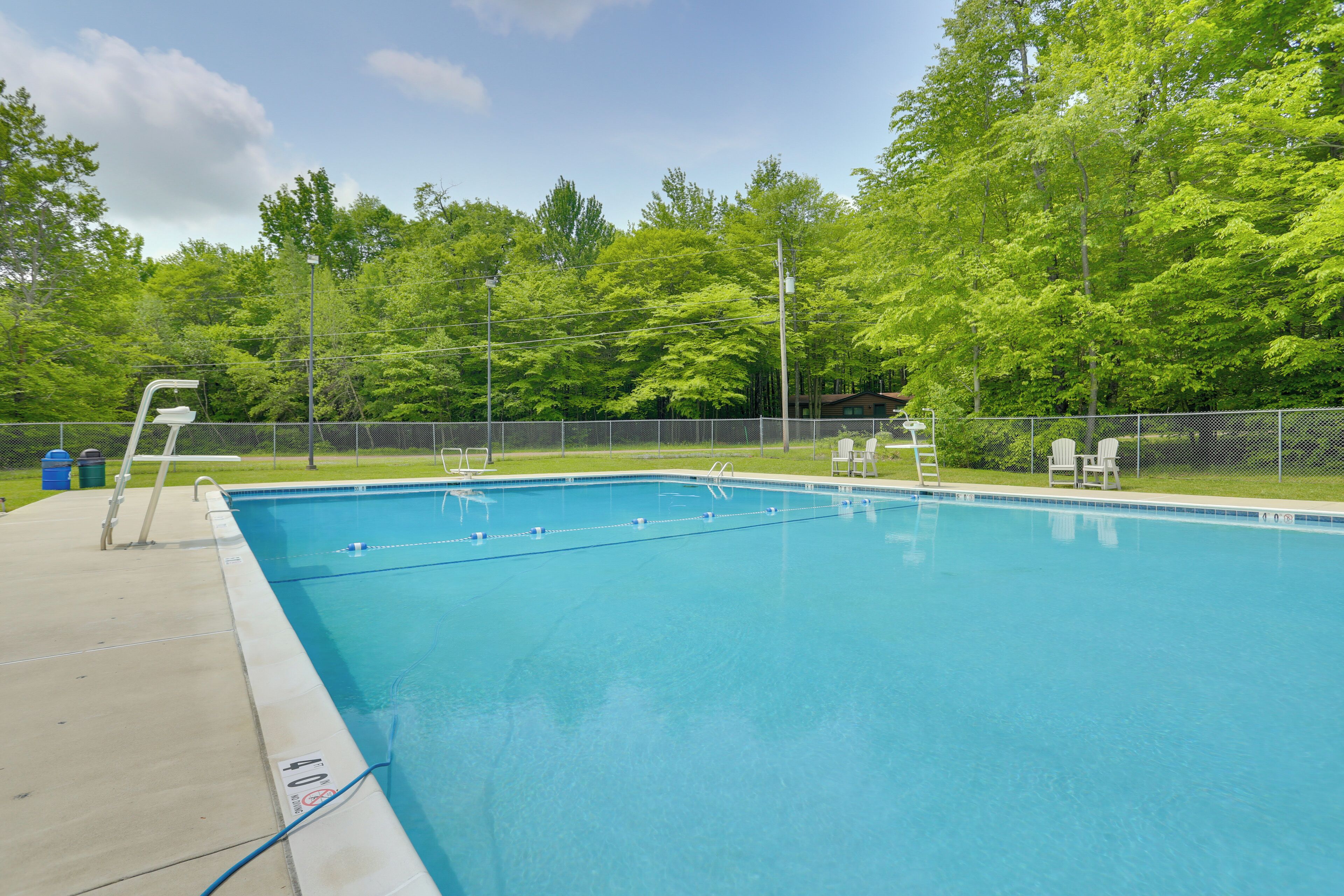 A rectangular swimming pool with a ladder on the left side, surrounded by a fence and trees.