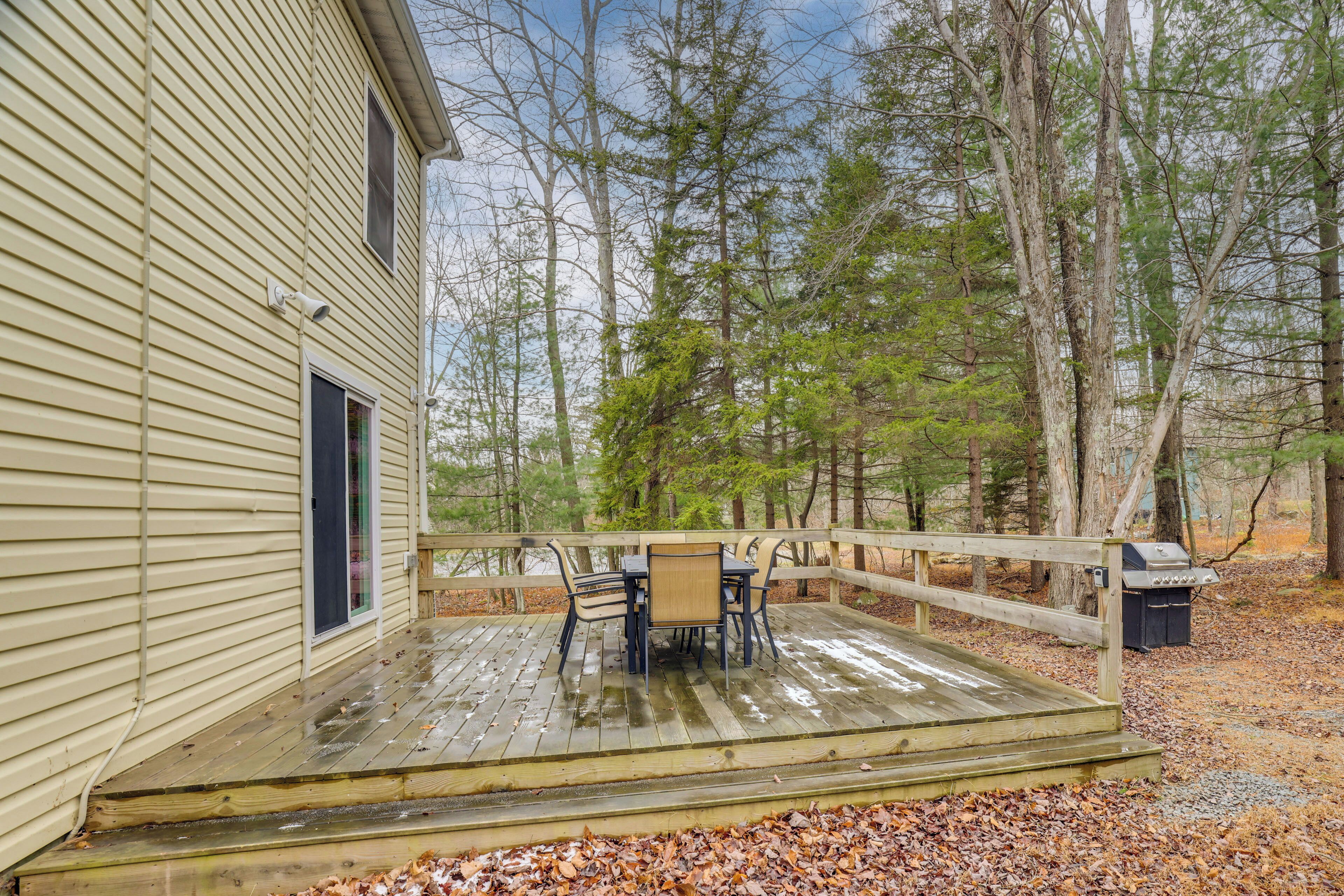 A wooden deck with a table and chairs, surrounded by a wooden fence and trees.