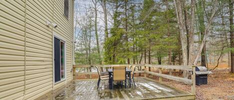 A wooden deck with a table and chairs, surrounded by a wooden fence and trees.