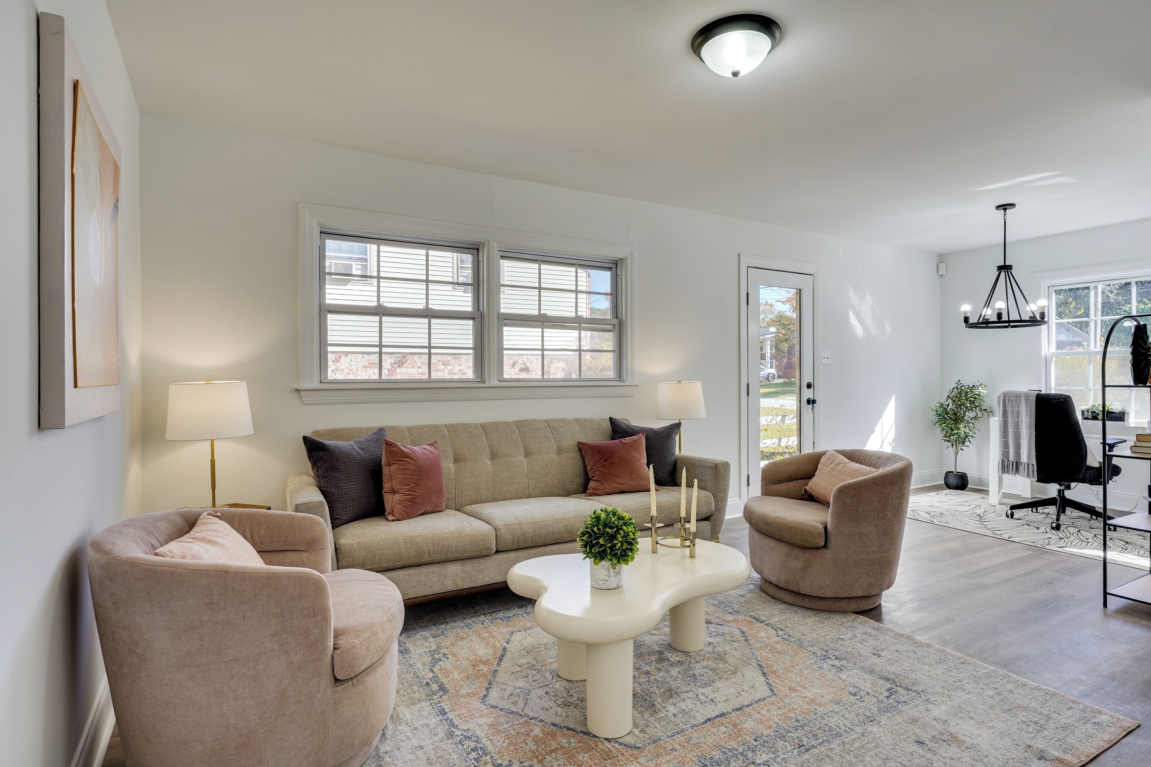 A modern living room with a beige sofa, two armchairs, a coffee table, and a chandelier.