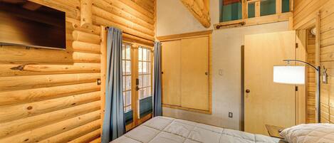 A log cabin room with a bed, a television, a wardrobe, and a window with curtains.