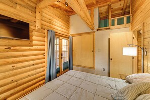 Una habitación tipo cabaña de madera con una cama, un televisor, un armario y una ventana con cortinas.