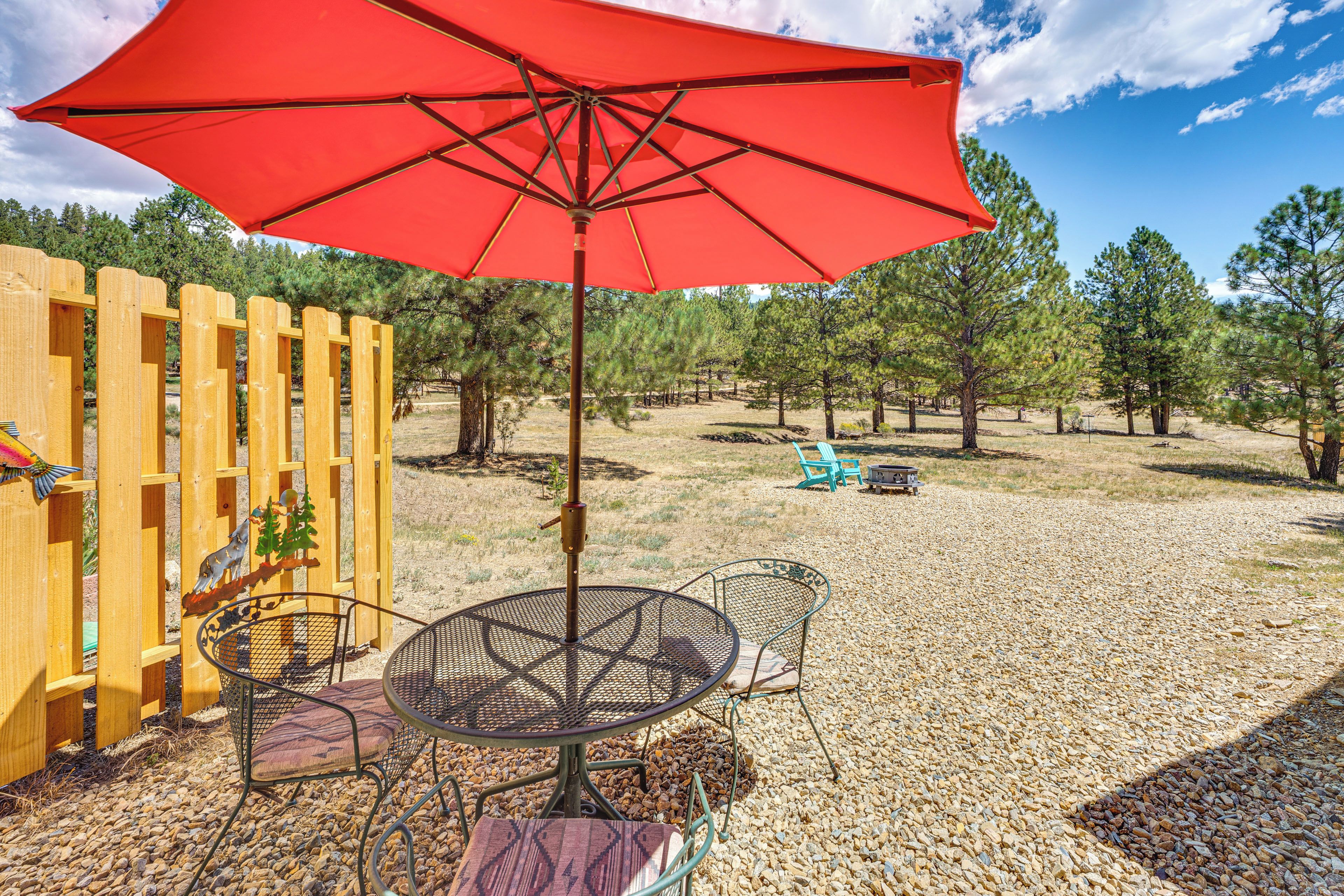 An outdoor seating area with a red umbrella, metal chairs, and a wooden fence.