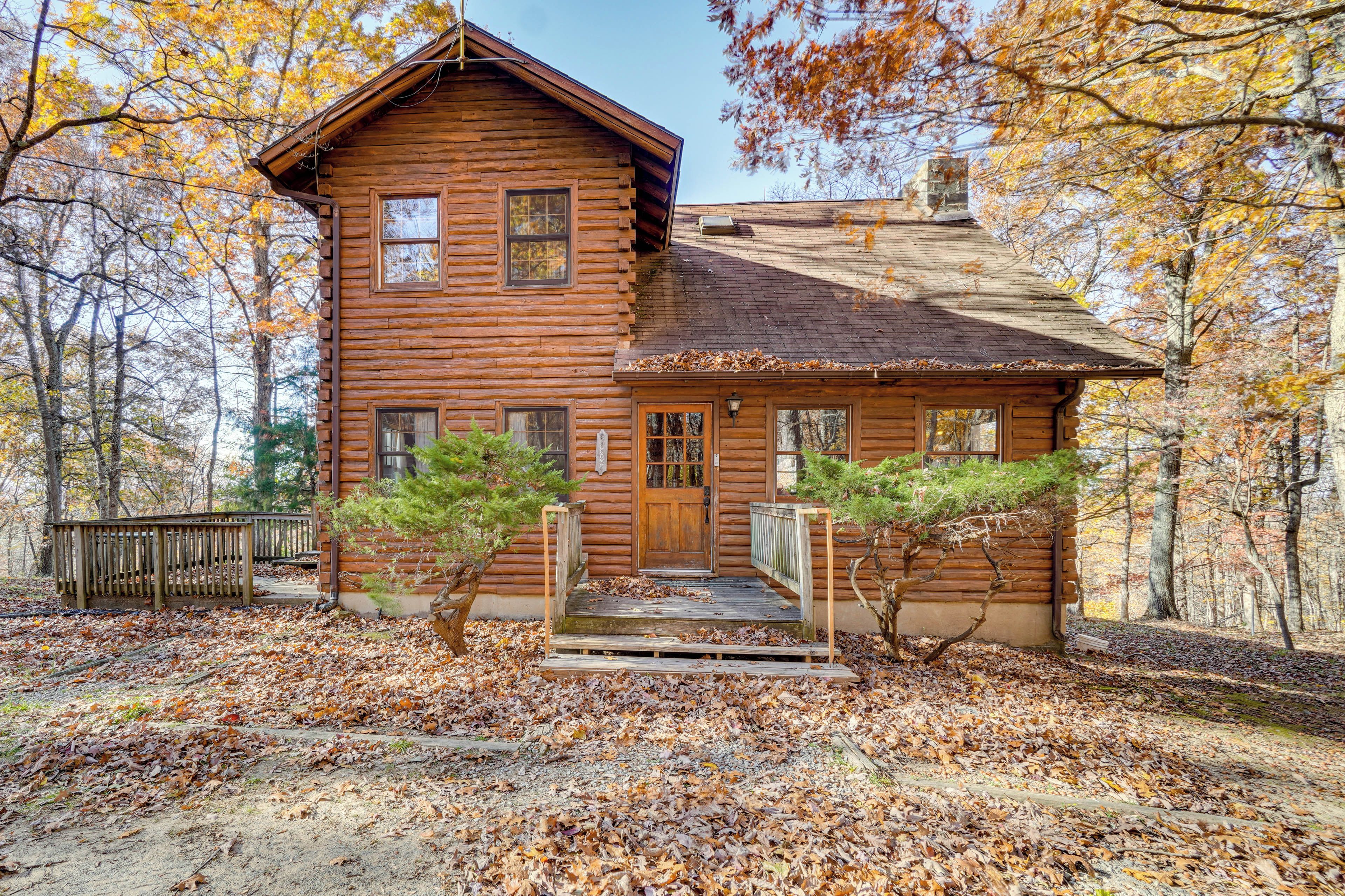 A log cabin with a wooden porch, a front door, and a small staircase leading up to the entrance.