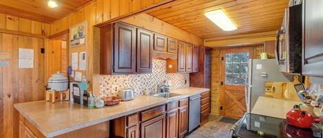 A wooden cabin kitchen with a large island, wooden cabinets, a refrigerator, and a stove.