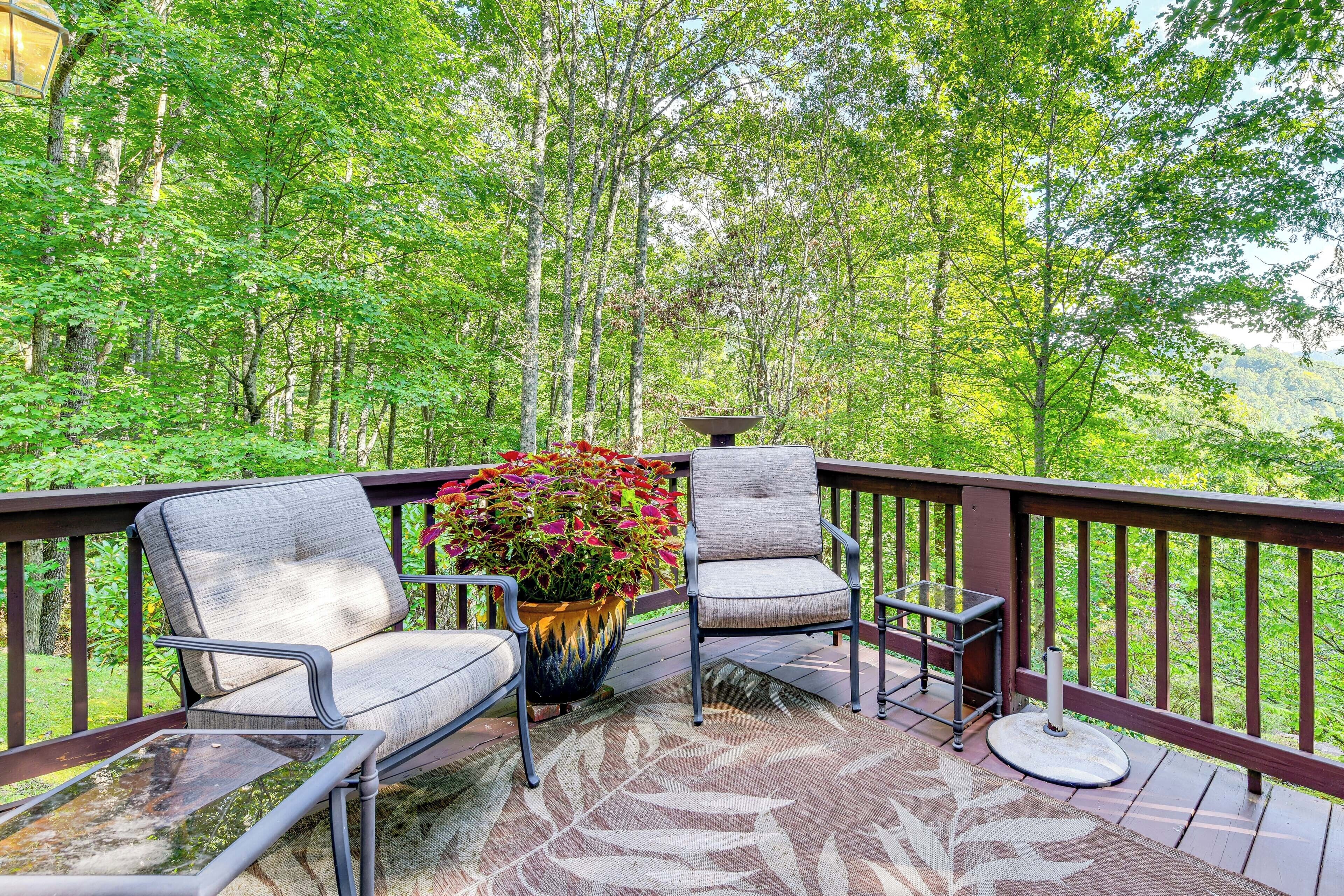 A deck with two chairs and a table, surrounded by a railing, overlooking a forested area.
