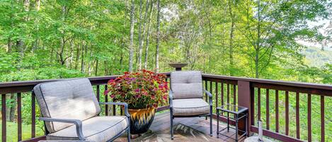 A deck with two chairs and a table, surrounded by a railing, overlooking a forested area.