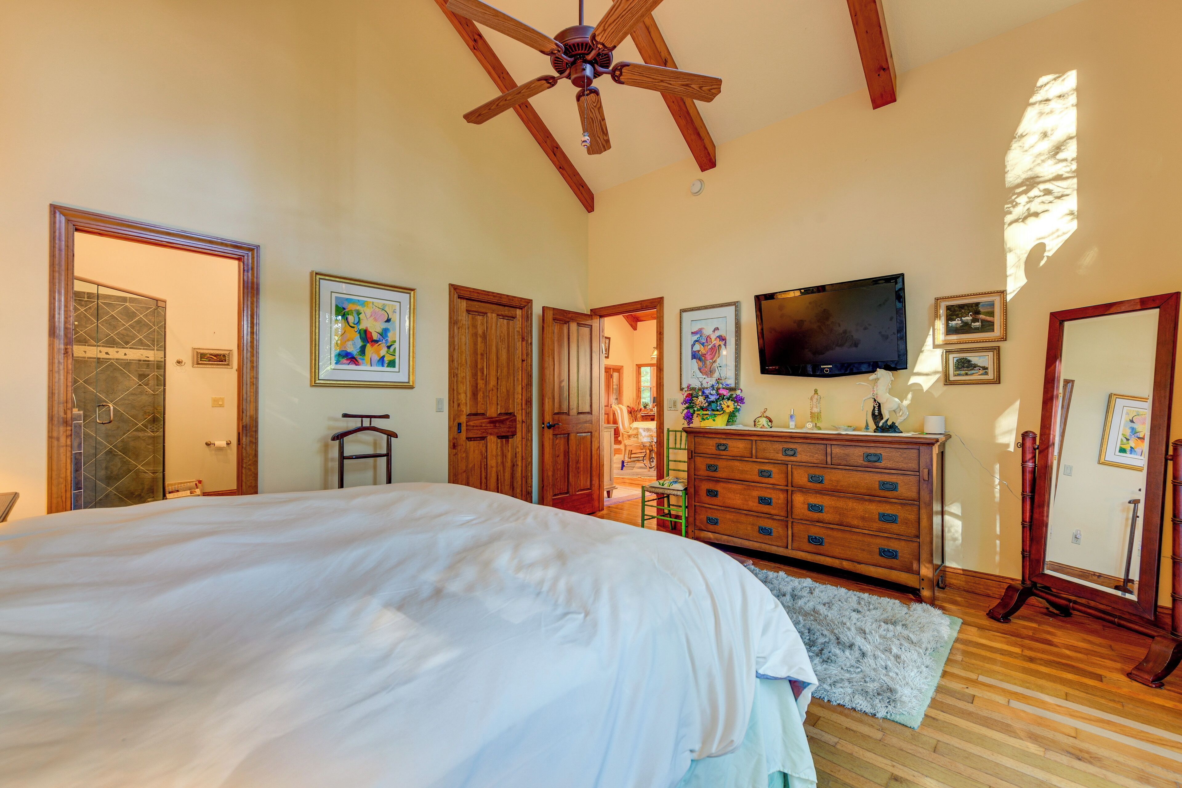 A bedroom with a large bed, wooden ceiling beams, a dresser, and a television.