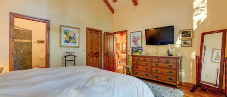 A bedroom with a large bed, wooden ceiling beams, a dresser, and a television.