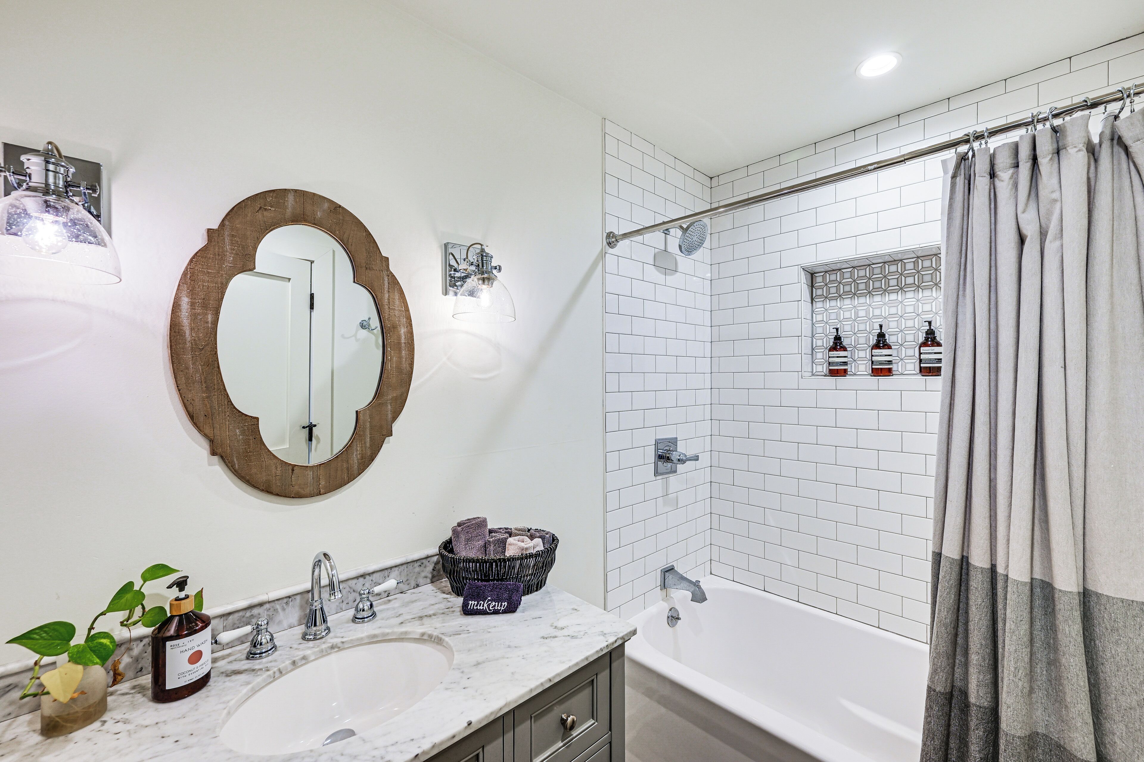 Un baño con lavamanos blanco, un espejo, ducha con cortina y artículos de aseo en la pared.