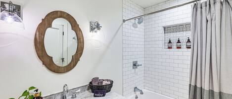 Un baño con lavamanos blanco, un espejo, ducha con cortina y artículos de aseo en la pared.