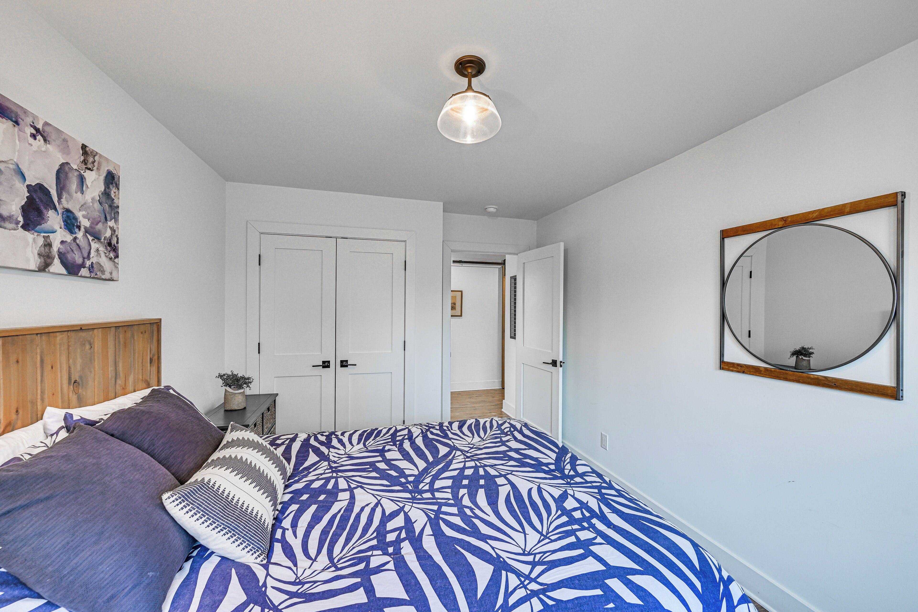 Une chambre à coucher avec un lit, un luminaire au plafond, une porte et un miroir fixé au mur.