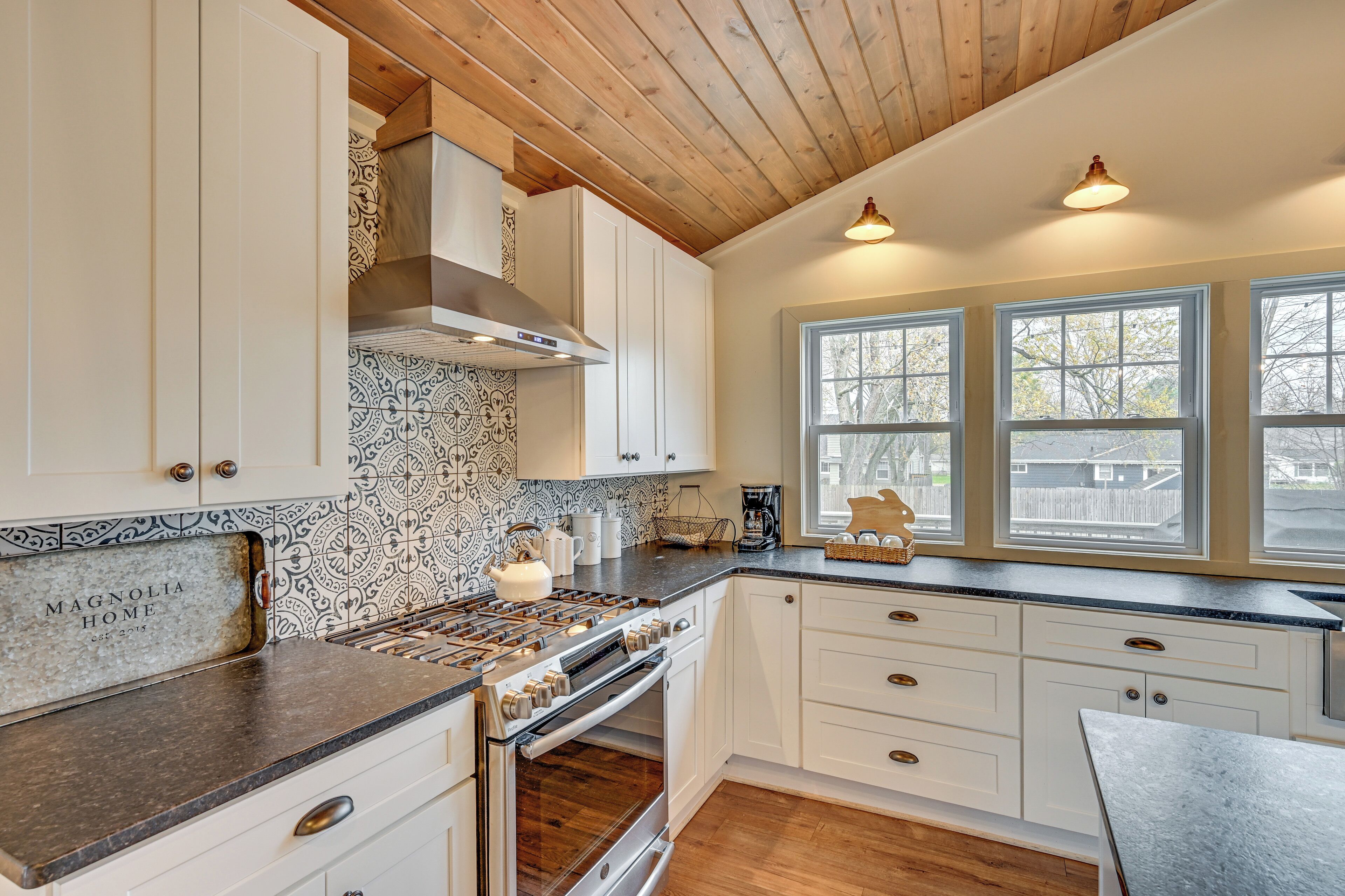 A kitchen with white cabinets, a patterned backsplash, a stove, and a window with a view of the outside.