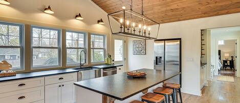 A modern kitchen with a large island, bar stools, and a wooden ceiling.