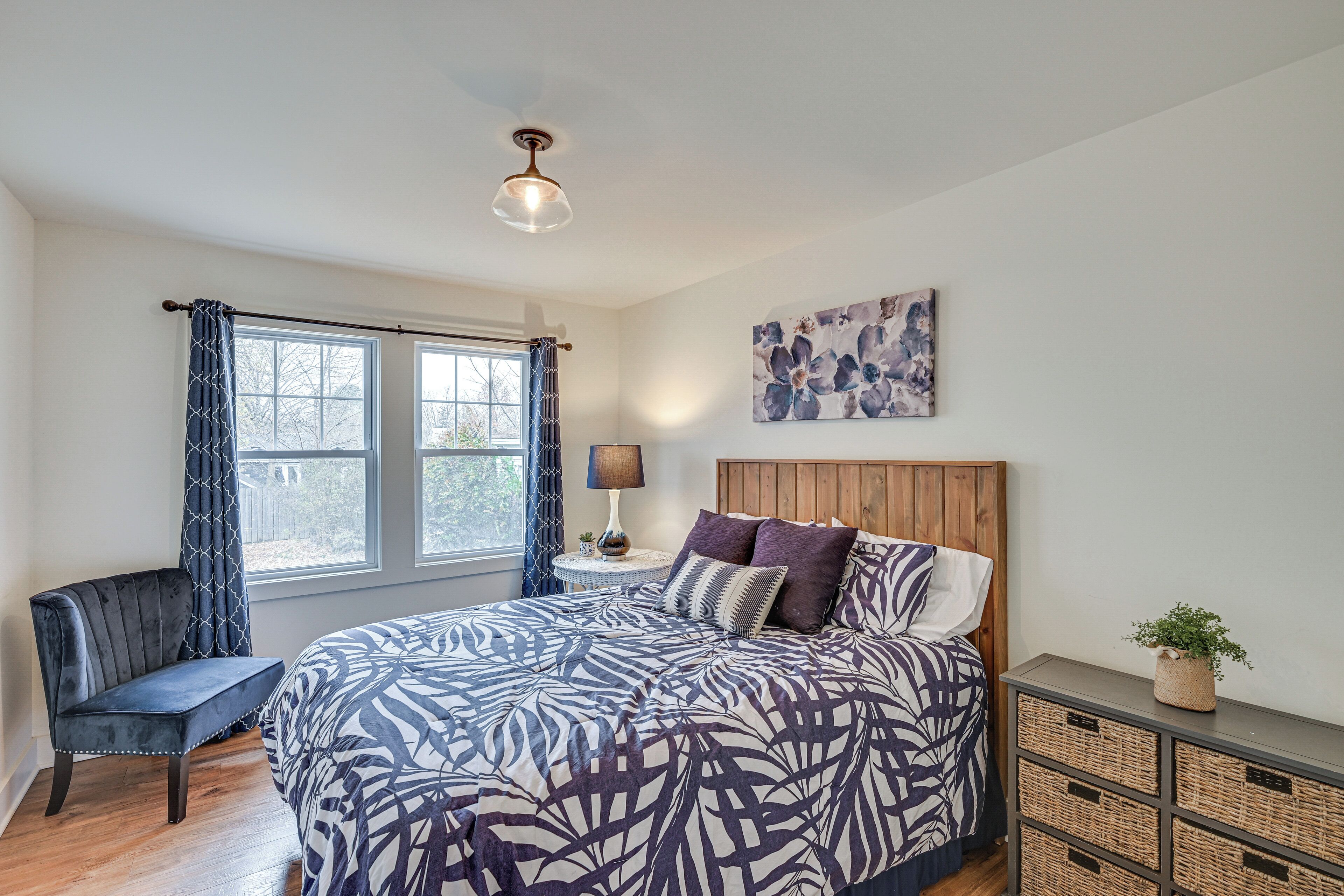 A bedroom with a large bed, a chair, a nightstand, a lamp, and a wall-mounted plant.
