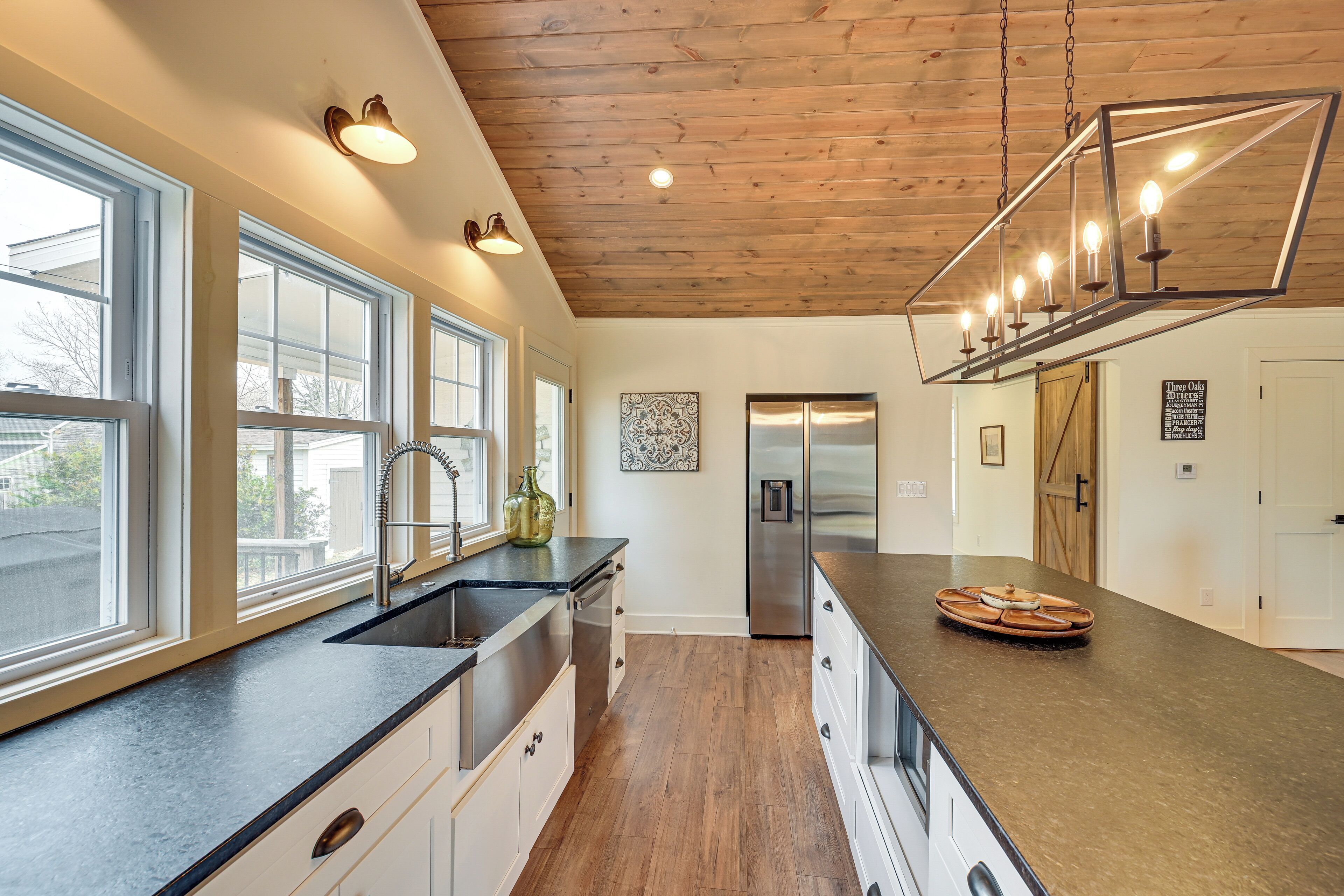 A modern kitchen with a large island, stainless steel appliances, and a wooden ceiling.