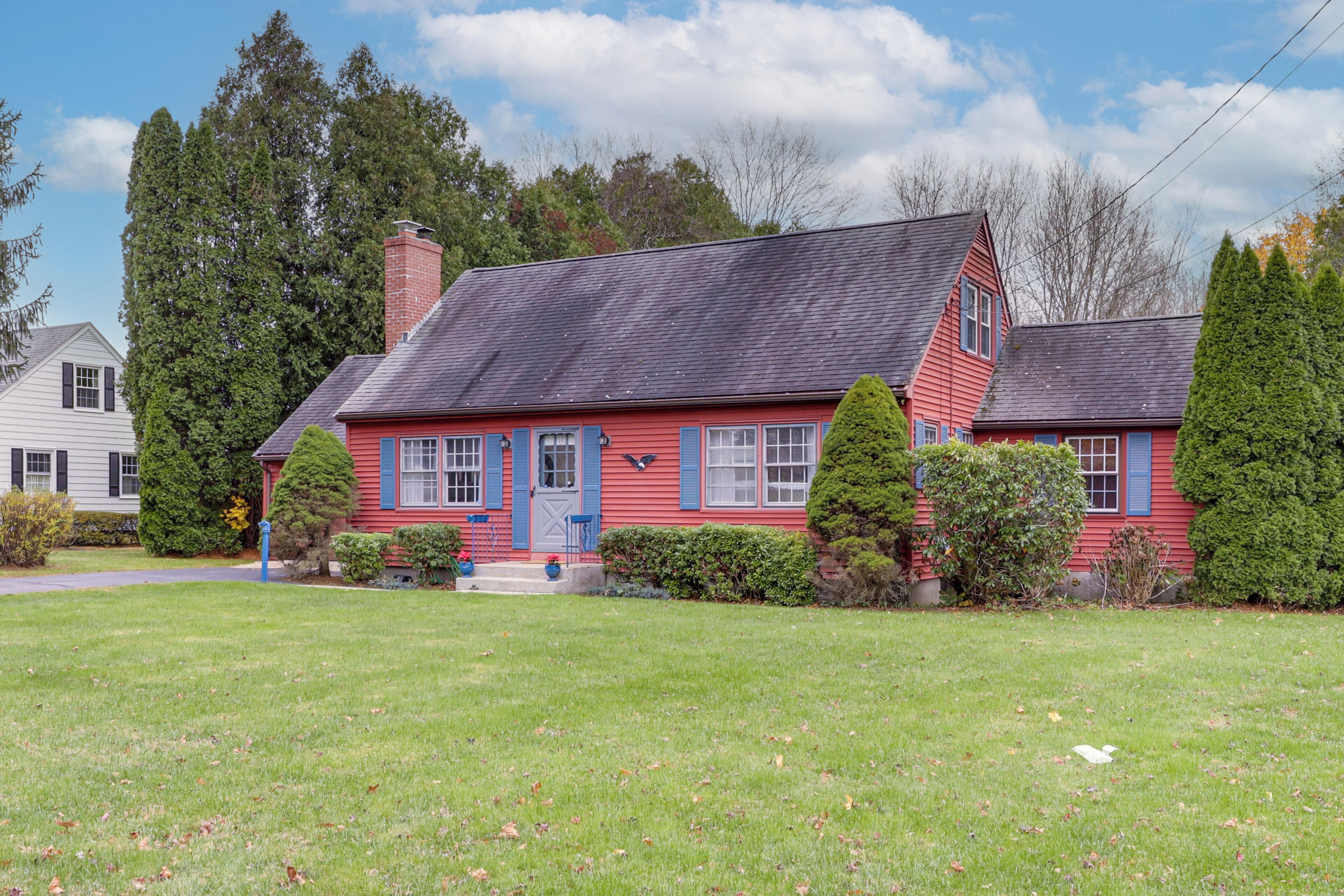 A red house with a grey roof, surrounded by a well-maintained lawn and tall trees.