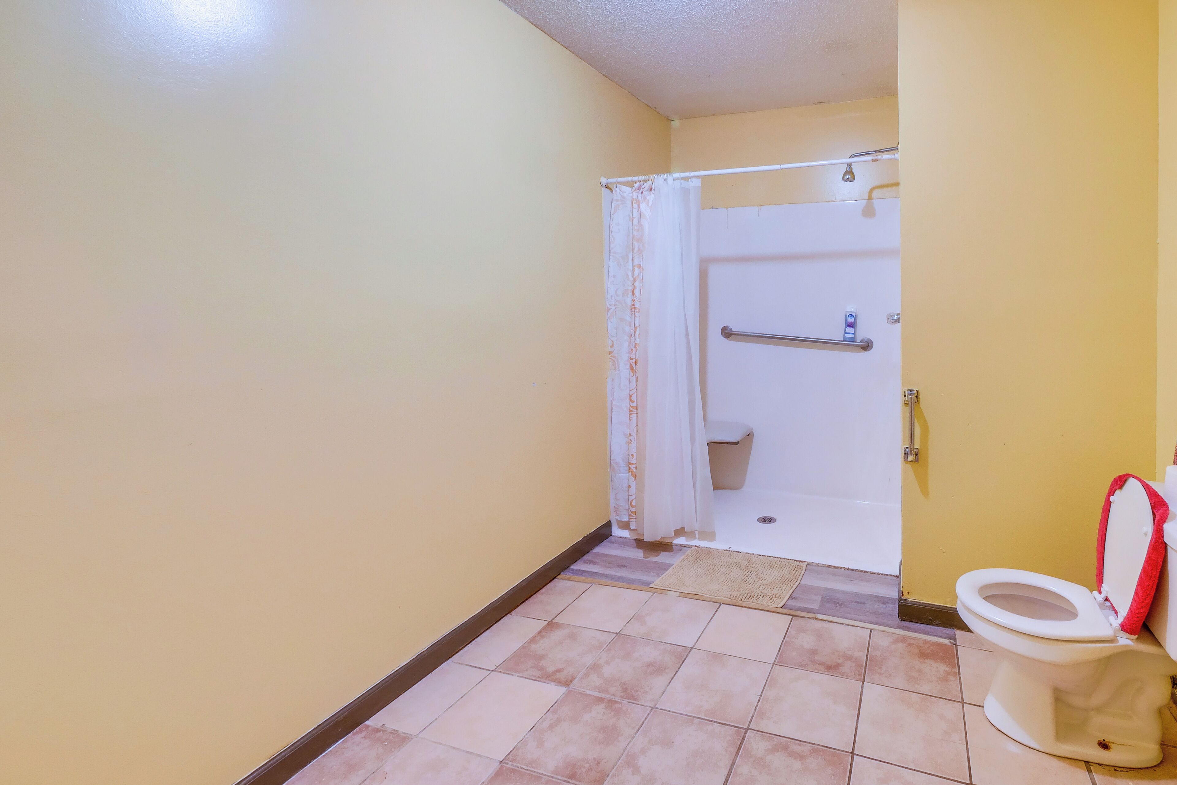 A bathroom with a toilet, a shower with a curtain, and a tiled floor.