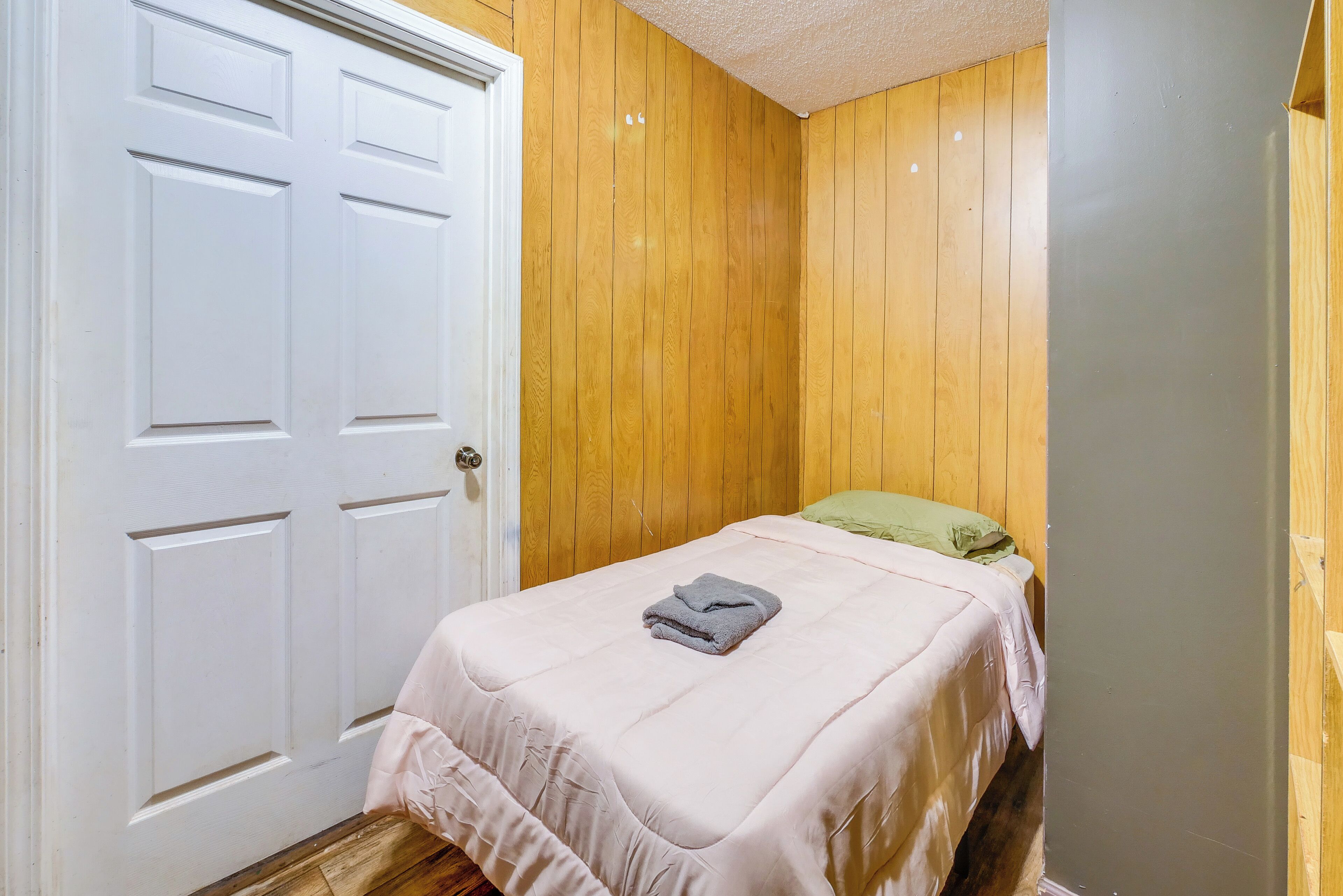 A bedroom with a single bed, a white door, and wooden walls.