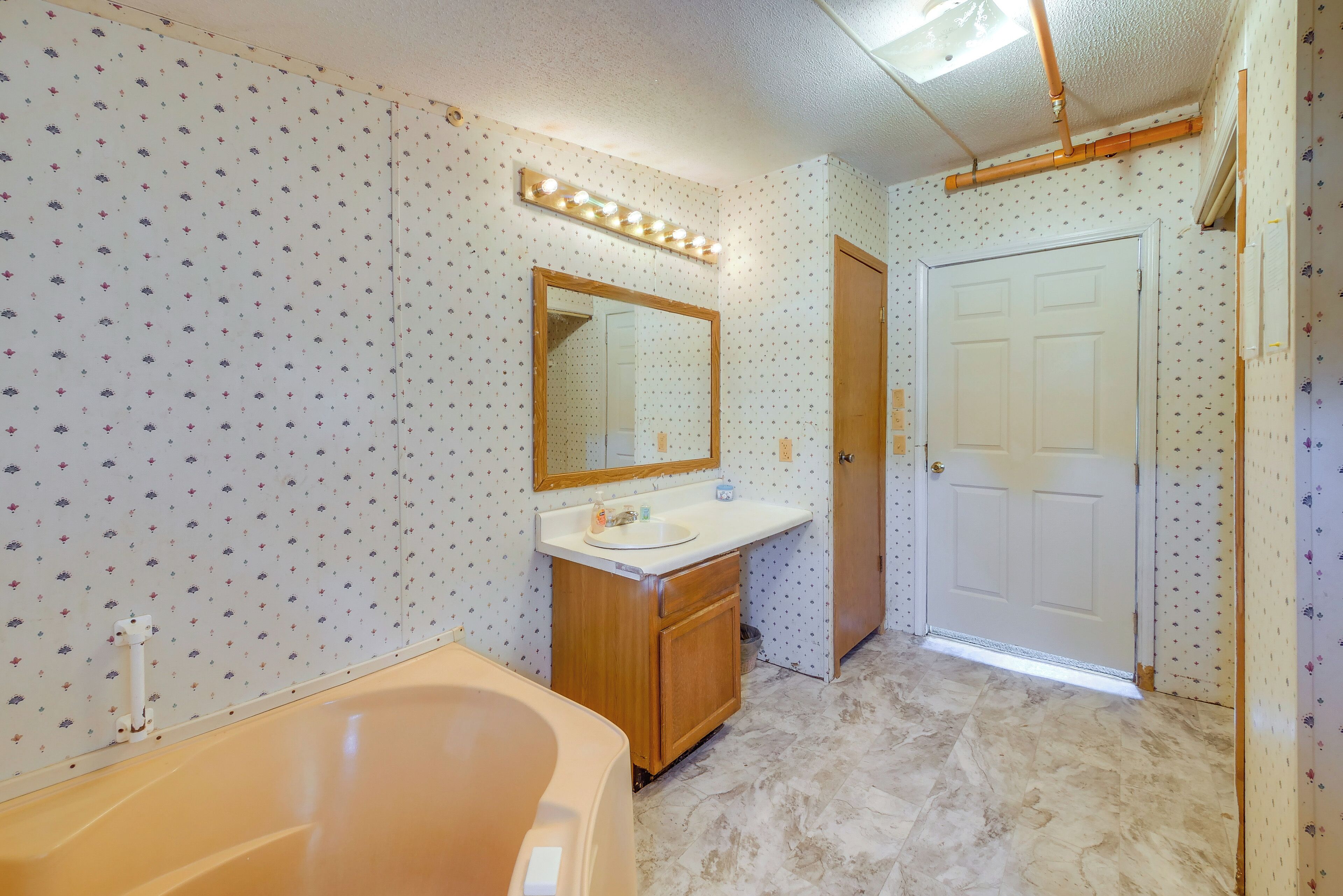 A bathroom with a bathtub, a vanity with a mirror and lights, and a door.