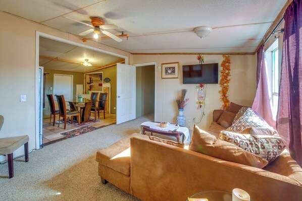 A cozy living room with a brown sofa, a dining table with chairs, a ceiling fan, and a TV mounted on the wall.