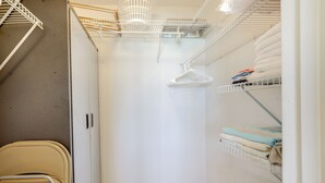 A compact storage closet with metal shelves, a white door, and a beige chair. - Steps to Shore: Ormond Beach Condo w/ Pool Access! (Ormond Beach)
