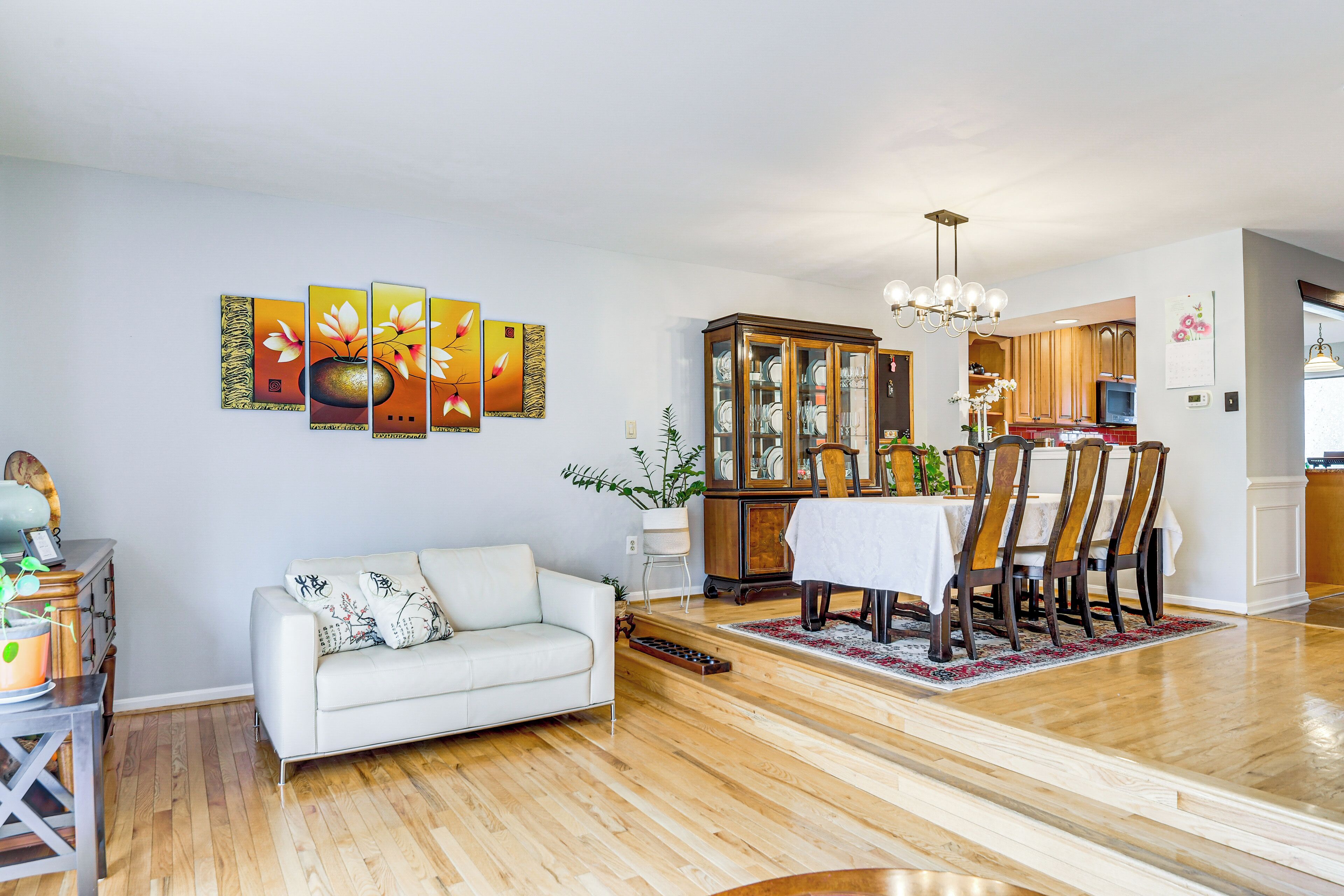 A spacious living room with a white sofa, wooden dining table, and a cabinet.