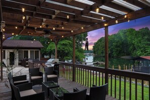 A covered outdoor deck with wicker furniture, a grill, and a view of a lake and trees. - Boaters Paradise on Lake Norman w/ Private Dock! (Terrell)