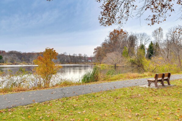 Un parc avec un banc au bord d’un lac, un chemin pavé et un feuillage automnal.