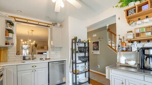 A modern kitchen with white cabinetry, a built-in dishwasher, and a central island. There is a black shelving unit with glass jars and a coffee machine. - Tranquil Townhouse Retreat w/ Deck in Germantown! (Germantown)