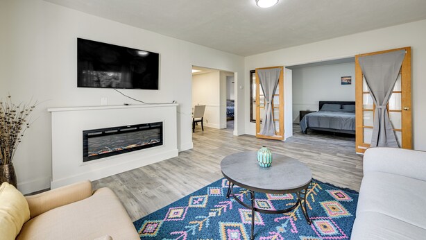 A modern living room with a fireplace, a television mounted above it, a round coffee table, and a colorful rug. - 3 Mi to Auburn Station! Commuter-friendly Home (Auburn)