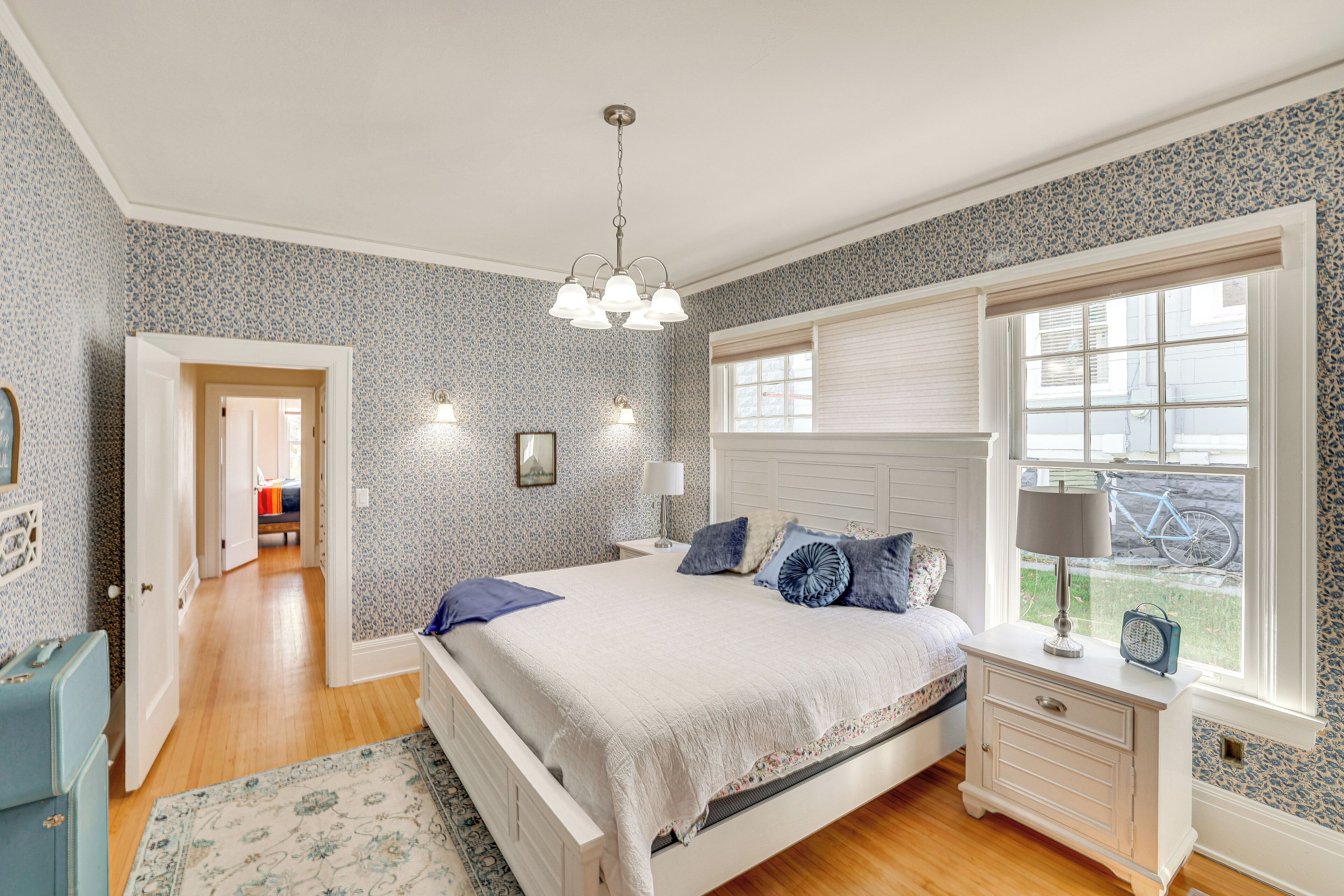 A bedroom with a large bed, a nightstand, a dresser, a window with blinds, and a view of the outside.