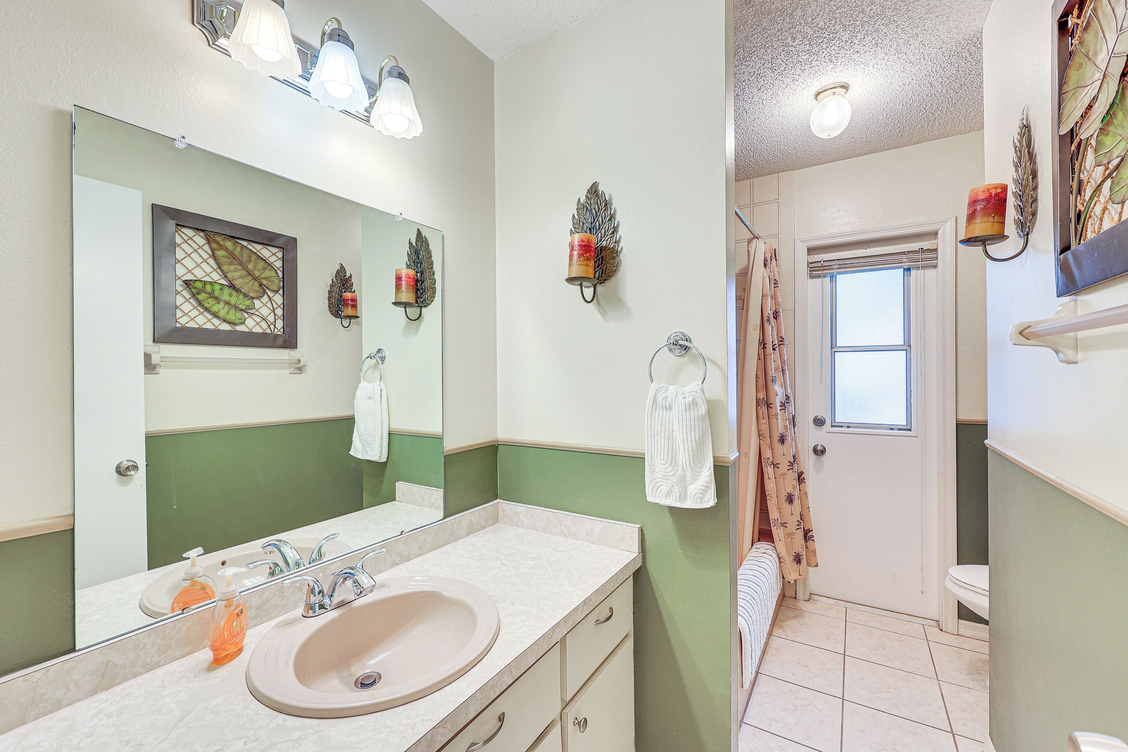A bathroom with a large mirror, two wall-mounted lights, a sink with a soap dispenser, and a towel hanging on a rack.